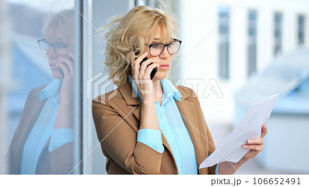 Businesswoman exits company building talking on smartphone Businesswoman exits company building talking on smartphone 106652491