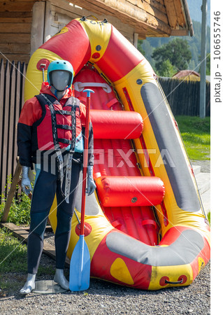 A mannequin in a red life jacket next to an inflatable boat as an advertisement for rafting or boating on the river in tourist places. A mannequin in a red life jacket next to an inflatable boat as an advertisement for rafting or boating on the river in tourist places. 106655746