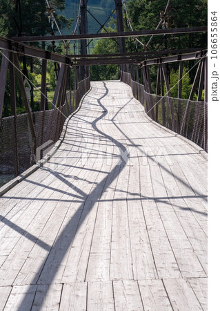 A wooden bridge with metal supports across a raging river in the Altai Mountains. Old broken bridge 106655864