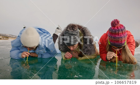 Siberia tradition cocktail Kiss of Baikal is entertainment for tourist on Lake Baikal.Three woman drink alcohol liquid without straw into makeshift glasses in hole frozen ice.Fun vacation trip travel. Siberia tradition cocktail Kiss of Baikal is entertainment for tourist on Lake Baikal.Three woman drink alcohol liquid without straw into makeshift glasses in hole frozen ice.Fun vacation trip travel. 106657819