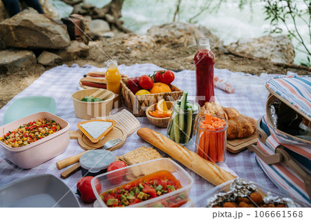 Picnic in the forest camping site with vegetables, juice, cheese, and croissants near mountain river. Fresh organic veggies surrounded with bread baguettes, salads Picnic in the forest camping site with vegetables, juice, cheese, and croissants near mountain river. Fresh organic veggies surrounded with bread baguettes, salads 106661568