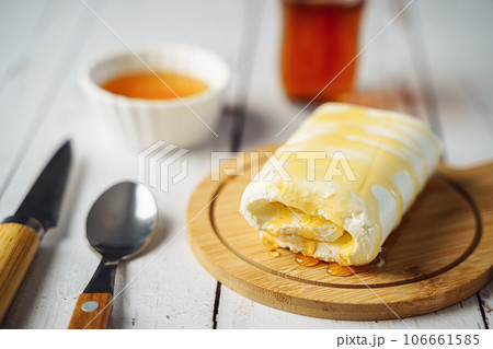 Close up picture of white cream milky kaymak butter roll poured with honey and tea on wooden plate 106661585