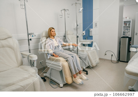 Pretty woman patient sitting in armchair while receiving IV infusion during treatment in hospital 106662997