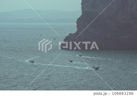 Long-tail boats go around a ledge of a limestone mountain, sailing on the evening sea. This is the route from Ao Nang Town to Railay Beach. Krabi Province, Thailand Long-tail boats go around a ledge of a limestone mountain, sailing on the evening sea. This is the route from Ao Nang Town to Railay Beach. Krabi Province, Thailand 106663286