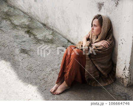 A girl in poor clothes sits on the ground A girl in poor clothes sits on the ground 106664746