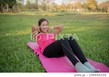 Asian woman exercising in the garden. She's doing sit-ups on the lawn. Asian woman exercising in the garden. She's doing sit-ups on the lawn. 106666208