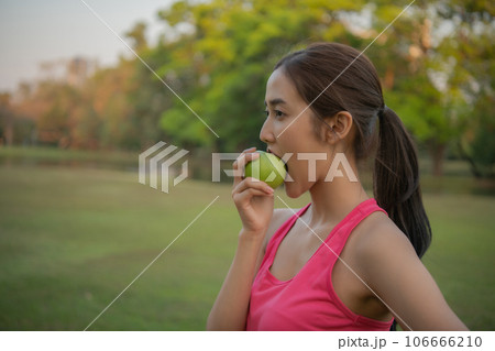Woman in sportswear eating healthy fruit. She is eating green apples to lose weight. 106666210