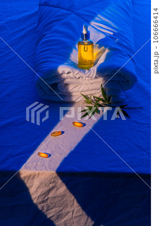 Bottle of CBD oil, and marijuana leaf on blanket podium in beam of moonlight 106666414