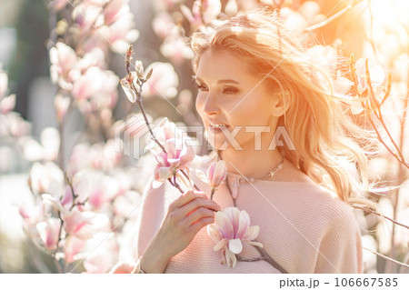 Magnolia woman portrait. Happy middle aged woman enjoying the smell in a blooming spring garden. Beautiful magnolia bushes, large flowers. 106667585