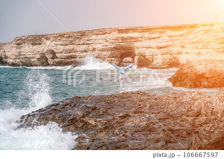 woman sea travel. A woman in a blue jacket stands on a rock above a cliff above the sea, looking at the stormy ocean. Girl traveler rests, thinks, dreams, enjoys nature woman sea travel. A woman in a blue jacket stands on a rock above a cliff above the sea, looking at the stormy ocean. Girl traveler rests, thinks, dreams, enjoys nature 106667597