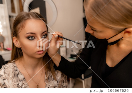 Make-up artist paints eyebrow pencil to beautiful brunette in be Make-up artist paints eyebrow pencil to beautiful brunette in be 106667626