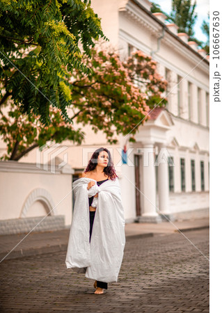 Woman city blanket. Morning in the big city. A blonde woman in a white blanket is enjoying in the city center. Photographed for social media Woman city blanket. Morning in the big city. A blonde woman in a white blanket is enjoying in the city center. Photographed for social media 106667630