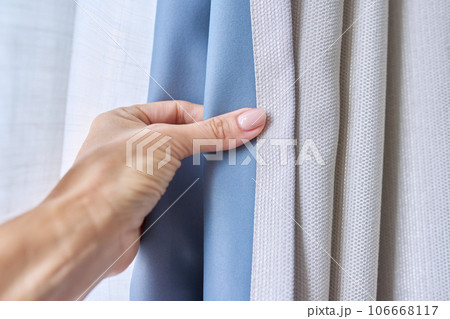 Woman's hand showing light gray curtain on blue opaque lining, fabric blackout Woman's hand showing light gray curtain on blue opaque lining, fabric blackout 106668117