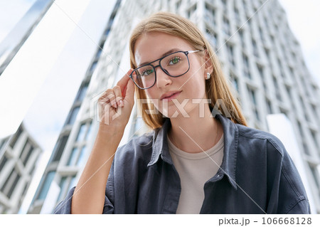 Teenage female in glasses looking at camera, glass skyscrapers background Teenage female in glasses looking at camera, glass skyscrapers background 106668128