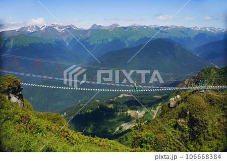 woman rouring walking on rope suspension bridge in caucasus mountains, Russia, Rosa Khutor resort 106668384