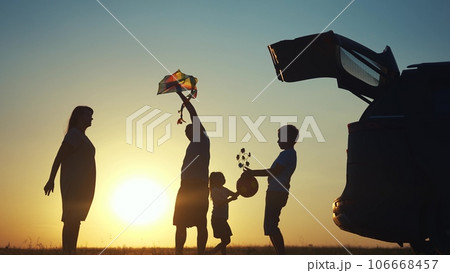 family traveling by car. family watching the sunset silhouette next to the car in the park. family playing kite ball. people in the park. family car lifestyle camping resting in nature 106668457