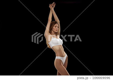 Portrait of young attractive woman posing in white color lingerie isolated over black background. 106669096