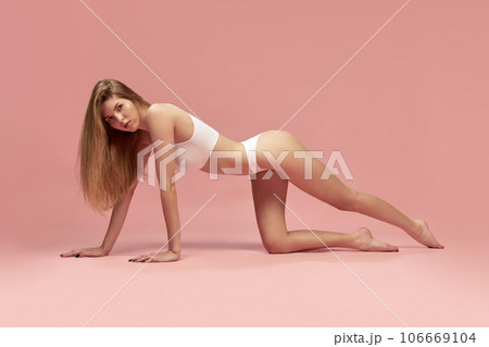 Charming young thin sportive woman in white cotton underwear posing on floor over pastel pink background. recretion, relaxing Charming young thin sportive woman in white cotton underwear posing on floor over pastel pink background. recretion, relaxing 106669104