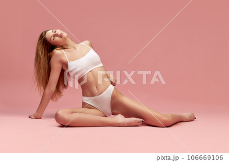 Relaxed young girl with fit, slim figure lying on floor, posing in underwear against pastel pink studio background 106669106