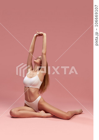 Charming young thin sportive woman in white cotton underwear sitting on floor over pink background. recretion, relaxing Charming young thin sportive woman in white cotton underwear sitting on floor over pink background. recretion, relaxing 106669107