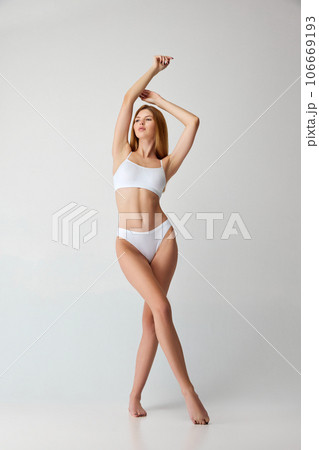 Full lenght portrait of beautiful young fit, slim woman in white underwear, lingerie posing against studio background. Full lenght portrait of beautiful young fit, slim woman in white underwear, lingerie posing against studio background. 106669193