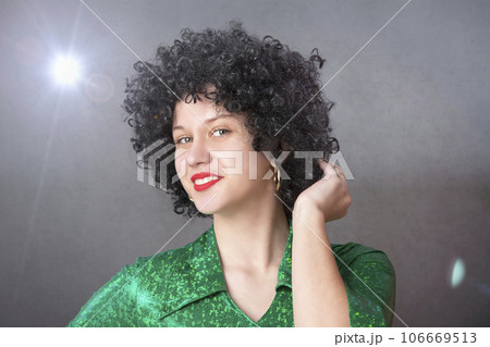 Excited woman in an afro wig on a gray background. Disco girl. 106669513
