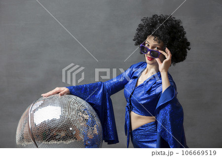 Girl with a disco ball in an afro wig on a gray background. Disco style from the seventies or eighties. 106669519