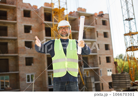 Construction site manager standing wearing safety vest. Man giving an order to workers. Construction site on a background. Construction site manager standing wearing safety vest. Man giving an order to workers. Construction site on a background. 106670301