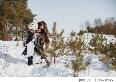 Cute girl walking in a winter park. Woman in a brown jacket. Lady with a dog. 106670435