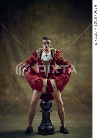 Emotional man, medieval royal person in female dress standing over giant chess piece against vintage green background. Game on 106670624