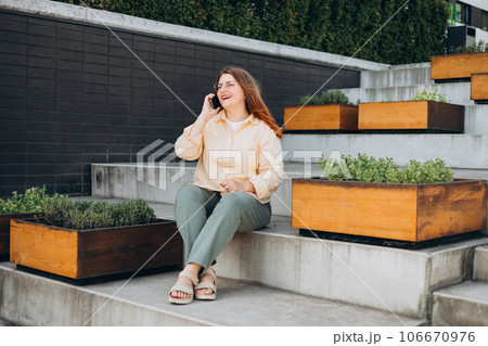 Lifestyle portrait of a stylish young 30s businesswoman talking on cell phone, making call and standing on modern city street. Successful small business. Urban lifestyle concept. Lifestyle portrait of a stylish young 30s businesswoman talking on cell phone, making call and standing on modern city street. Successful small business. Urban lifestyle concept. 106670976