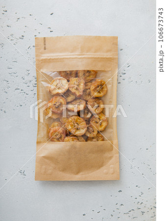 Pack of dried bio organic healthy banana chips on light board.Macro 106673743