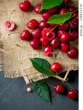 Sweet red cherry on burlap on a black background. A large number of cherries with leaves on the table, on a black background. close-up. Sweet red cherry on burlap on a black background. A large number of cherries with leaves on the table, on a black background. close-up. 106674146