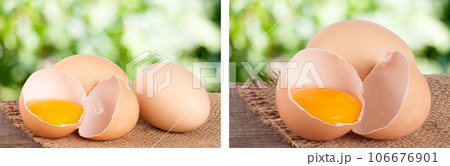 Broken egg with yolk and eggshell On a wooden table with a blurry garden background 106676901