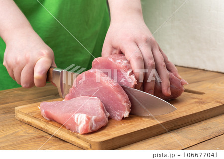 A girl cuts pork meat into pieces using a knife on a cutting board. 106677041
