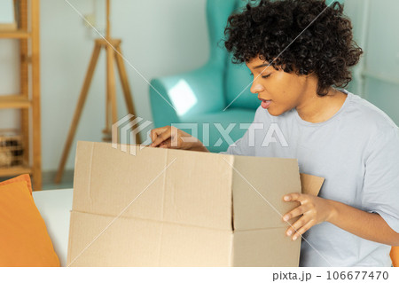 African girl unpacking delivery looking in box. Happy woman opening carton box. Female getting parcel looking at delivered goods items. Satisfied client positive feedback quick express deliver African girl unpacking delivery looking in box. Happy woman opening carton box. Female getting parcel looking at delivered goods items. Satisfied client positive feedback quick express deliver 106677470