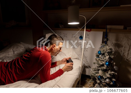 young man in christmas pyjama in bed watching a tablet 106677605