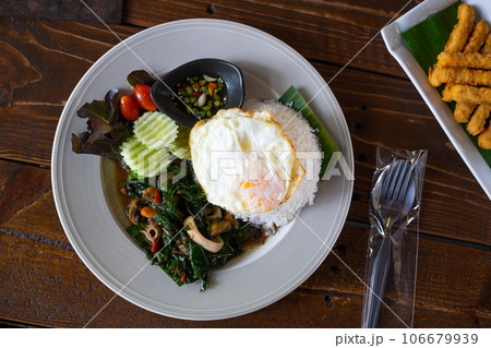 Stir-Fried Basil and Seafood with Fried Egg on the Wood Table in the Restureant, Delicious Gourmet with Spicy and Tasty Stir-Fried Basil and Seafood with Fried Egg on the Wood Table in the Restureant, Delicious Gourmet with Spicy and Tasty 106679939