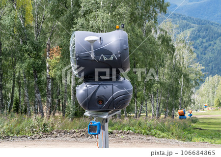 Yellow snow cannon on the edge of a hill overlooking a valley in summer or warm winter, green mountain peaks. Ski slope without snow in summer or during warm winter, greenhouse effect concept. Yellow snow cannon on the edge of a hill overlooking a valley in summer or warm winter, green mountain peaks. Ski slope without snow in summer or during warm winter, greenhouse effect concept. 106684865