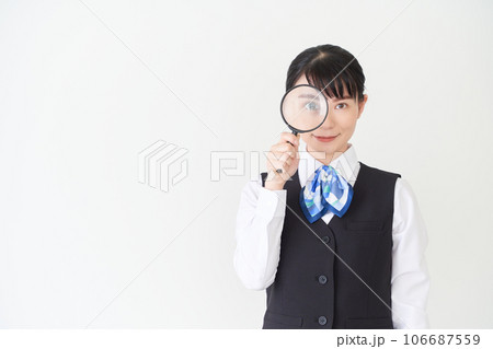 虫眼鏡を持つベストにリボンタイの制服を着た、受付業務、事務業務の女性 虫眼鏡を持つベストにリボンタイの制服を着た、受付業務、事務業務の女性 106687559