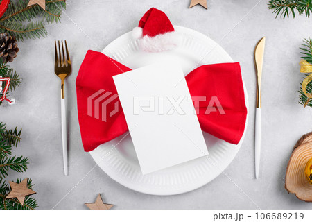 Christmas table setting with greeting card mockup on red napkin with gold cutlery, top view 106689219
