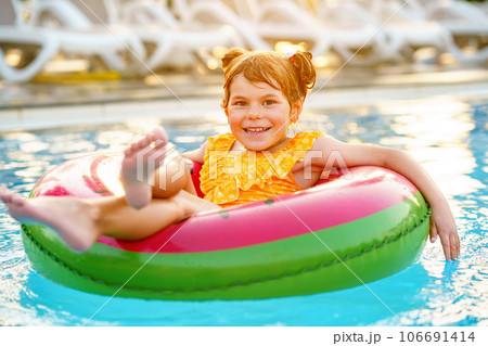 Happy little girl with inflatable toy ring float in swimming pool. Little preschool child learning to swim and dive in outdoor pool of hotel resort. Healthy sport activity and fun for children. Happy little girl with inflatable toy ring float in swimming pool. Little preschool child learning to swim and dive in outdoor pool of hotel resort. Healthy sport activity and fun for children. 106691414