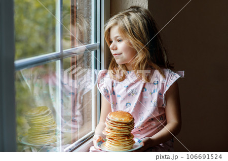 Little happy preschool girl with a large stack of pancakes for breakfast. Positive child eating healthy homemade food in the morning. 106691524