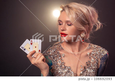 Blonde woman with a beautiful hairstyle and perfect make-up is posing with playing cards in her hands. Casino, poker. 106692093