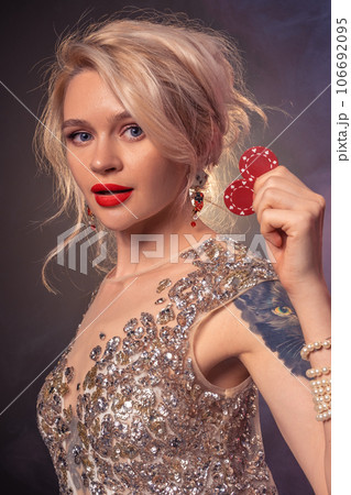 Blonde woman with a beautiful hairstyle and perfect make-up is posing with red gambling chips in her hands. Casino, poker. 106692095