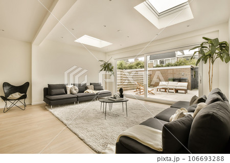 a living room with wood flooring and skylights on the ceiling, there is a black sofa in front a living room with wood flooring and skylights on the ceiling, there is a black sofa in front 106693288