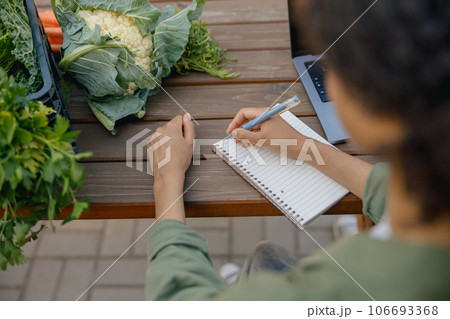 Close up of woman farm owner making notes in notepad with vegetables on background 106693368