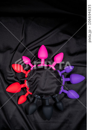 A set of silicone anal plugs in different colors and sizes on a black silk sheet.  106694835