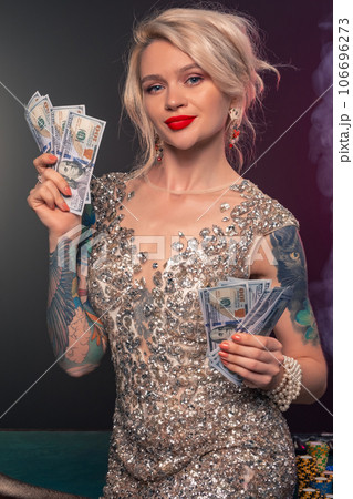 Blonde woman with a beautiful hairstyle and perfect make-up is posing with some money in her hands. Casino, poker. 106696273