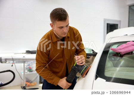 Man polishing his luxury sport car with applicator pad grinder in garage 106696944